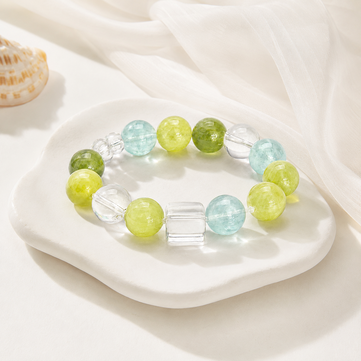 Peridot and crystal stretch bracelet on white ceramic tray with seashell